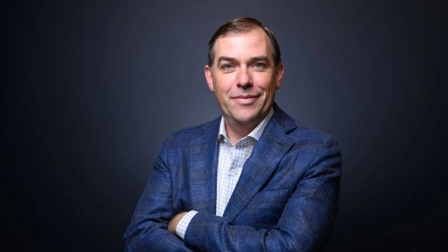 Matt Garman wearing a blue jacket with his arms crossed against a dark background