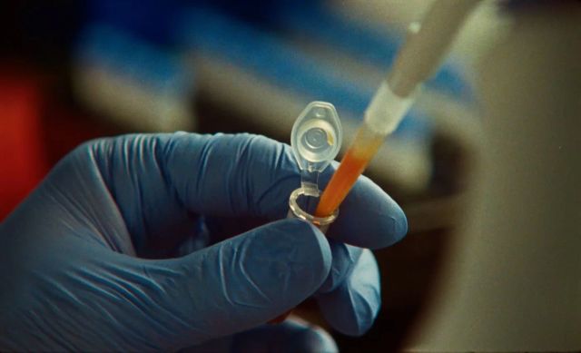 Gloved hand holding a small lab tube beneath a pipette